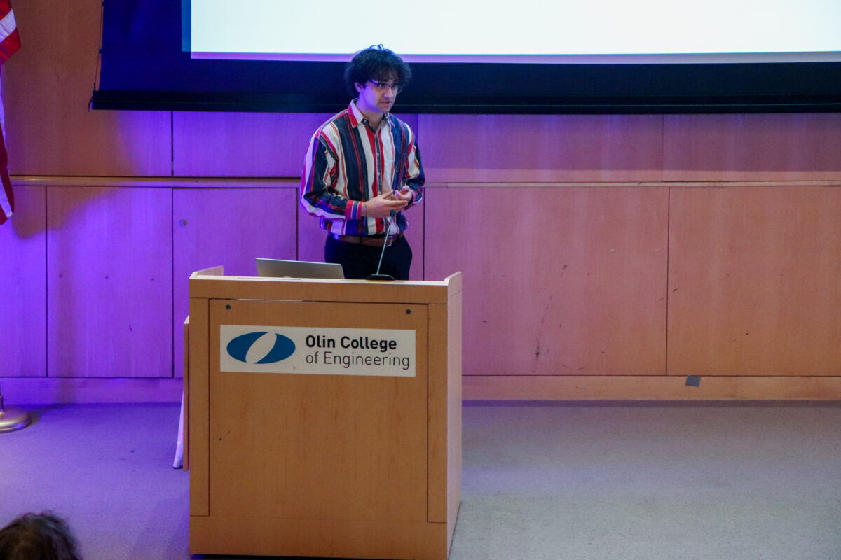 Alex Butler, student at Olin College of Engineering, at a podium presenting his final project.