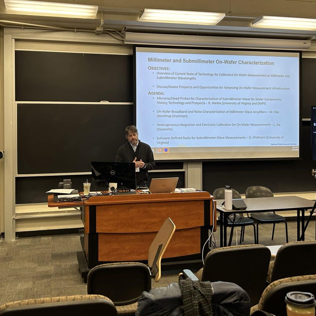 Bobby Weikle, SpectrumX Steering Committee Chair and Radio and Network Technologies Lead, and Professor at University of Virginia, held a workshop at NRSM 2023 on device and circuit characterization at millimeter and submillimeter bands above 100 GHz. Bobby stands at the front of a classroom, at a podium, presenting.