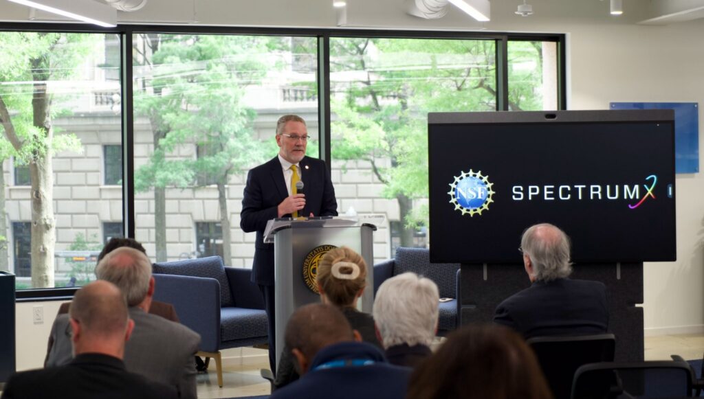 Nick Laneman uses a microphone to speak to a crowd behind a podium