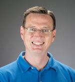 A white man in glasses and a blue polo shirt smiles