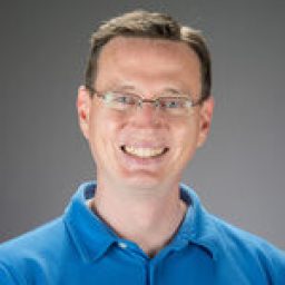 A white man in glasses and a blue polo shirt smiles